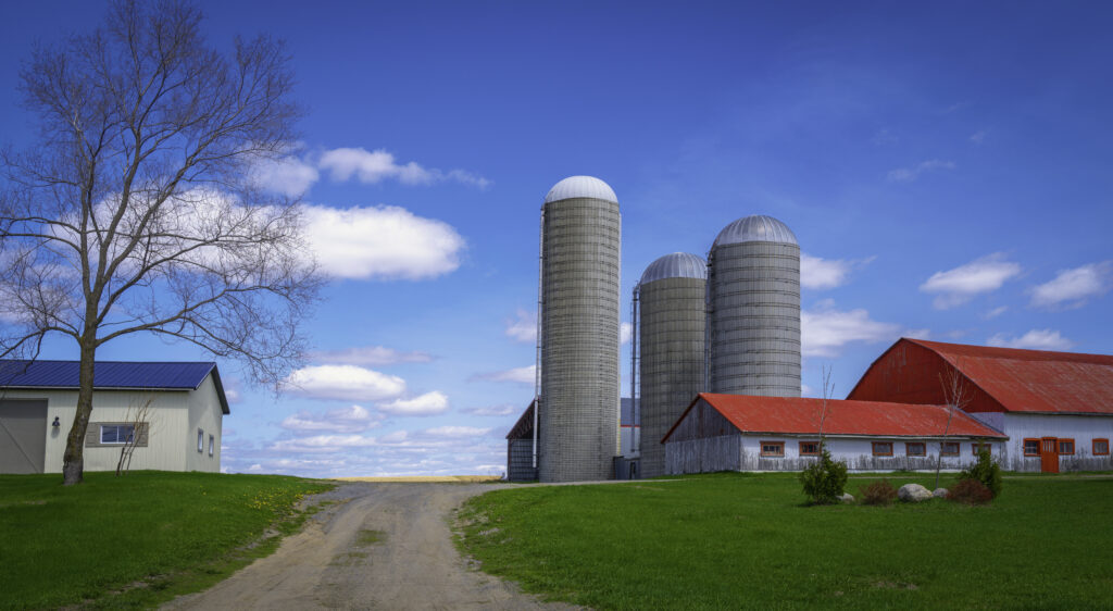 Tranquil countryside landscape with white clouds, tall silos, rustic red rooftop houses, and a white barn over the green hill